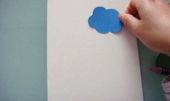 将蓝色云朵的彩纸片用胶棒粘贴在硬纸卡上面